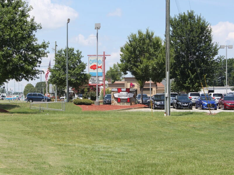 Green lawn with car dealership signs and vehicles in background.